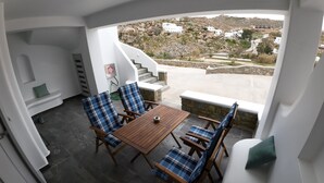 Un balcon avec une table en bois et des chaises à carreaux bleus, donnant sur un paysage rocheux parsemé de bâtiments blancs.