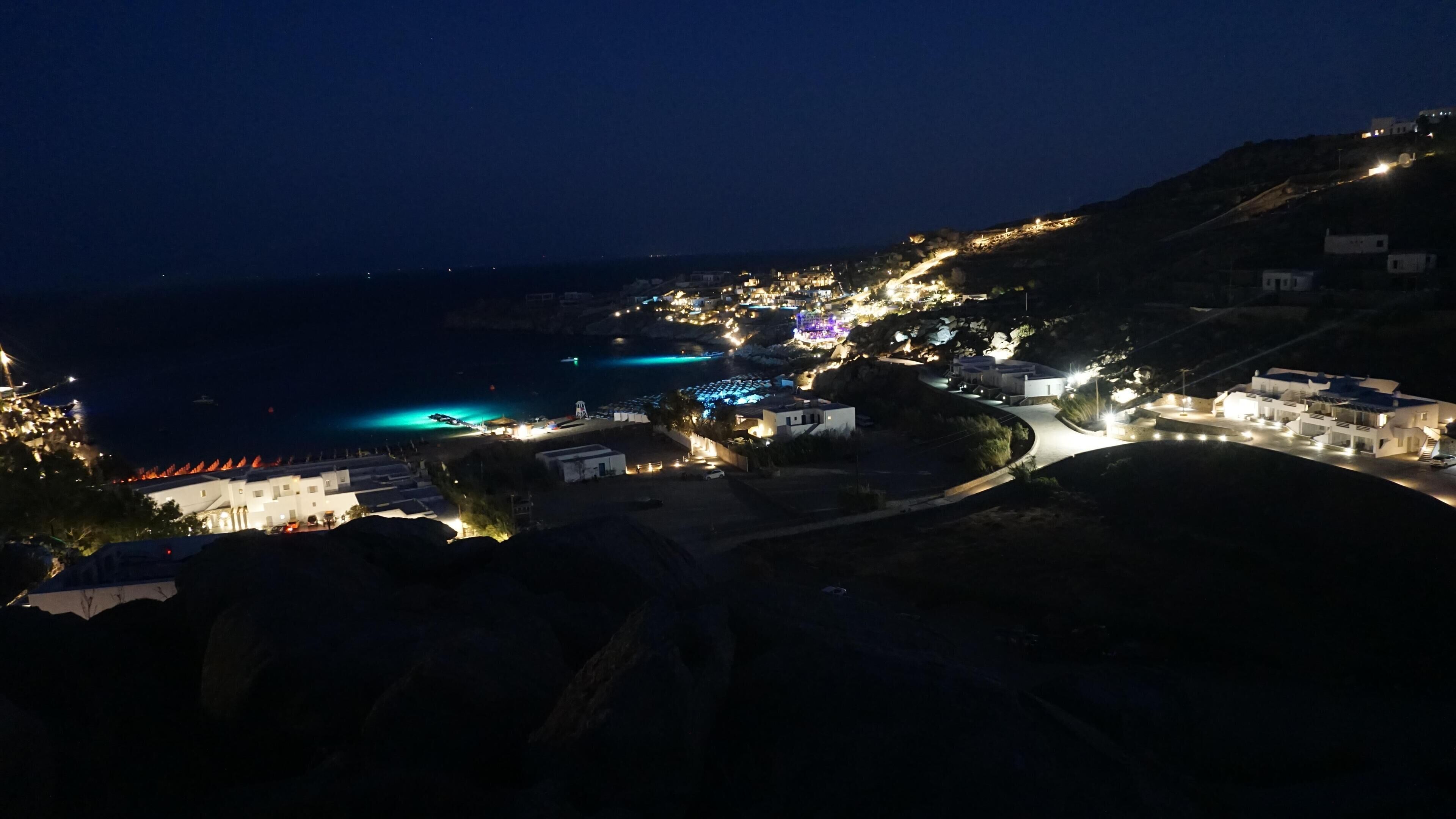 Un poble costaner de nit amb edificis il·luminats i un camí sinuós.
