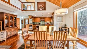 Un comedor amplio con una mesa y sillas de madera, una cocina al fondo y un ventanal con vistas al exterior.