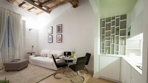 Een moderne woonkamer met een bank, eettafel en stoelen, een klein bijzettafeltje en een boekenkast met glazen.