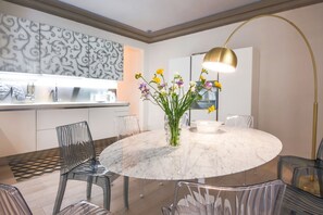A modern dining area with a marble table, clear chairs, and a vase of flowers.
