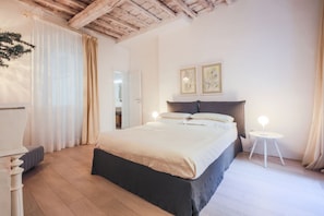 A bedroom with a bed, bedside tables, a ceiling with exposed beams, and a door leading to another room. - Apartments Florence - Boboli Deluxe (Firenze)