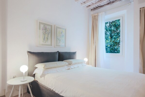 A bedroom with a bed, two bedside tables, and a window with curtains.