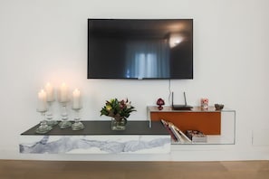 A modern living room with a marble console table, a flat-screen TV mounted on the wall, a glass cabinet with decorative items, and a vase with flowers. - Apartments Florence - Boboli Deluxe (Firenze)