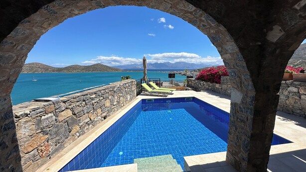 Ein Pool mit Steinwänden und unendlich wirkendem Überlauf, mit freiem Blick auf das Meer und die Berge.