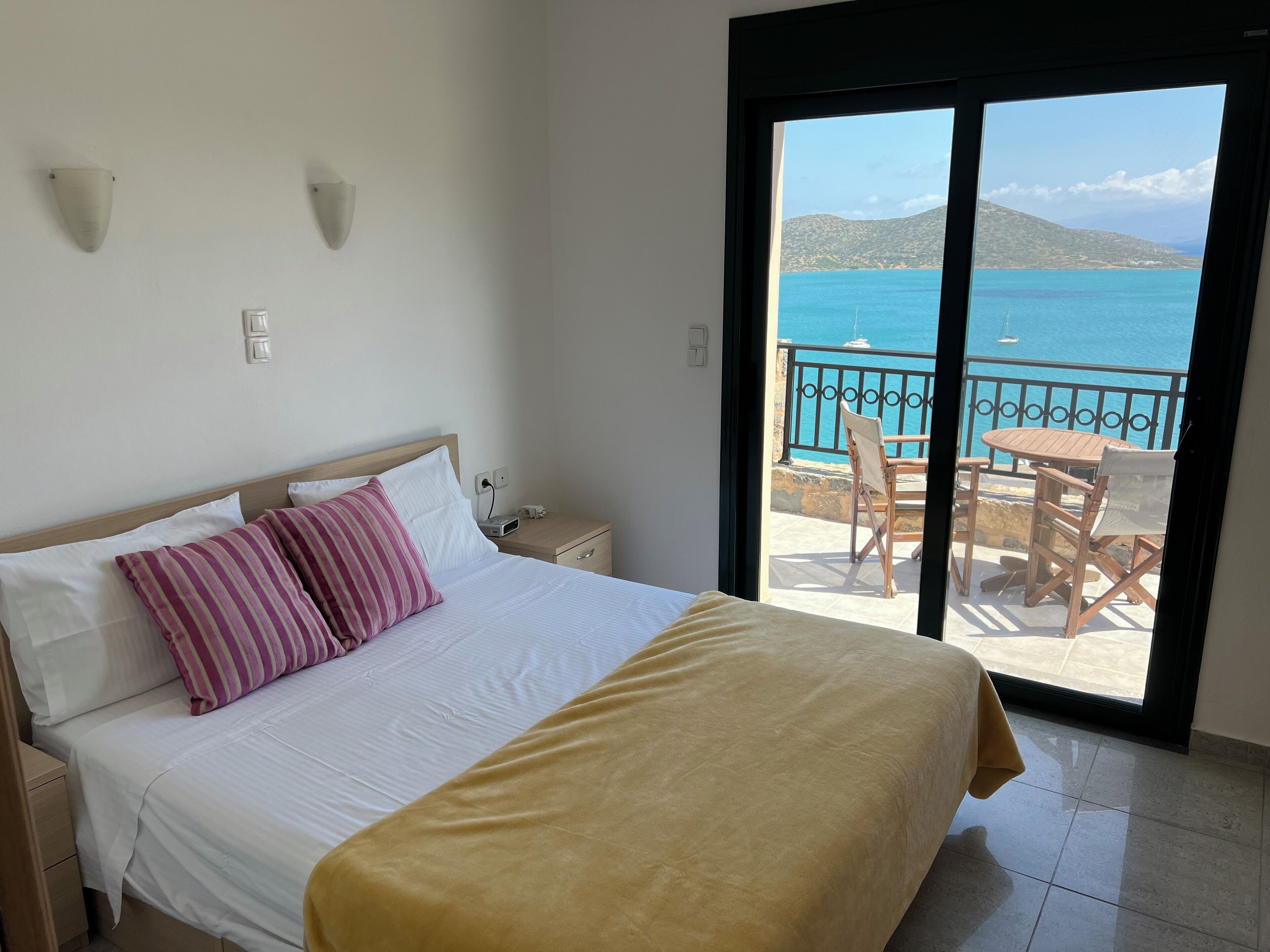 Une chambre d’hôtel avec un lit, une table de chevet, une prise de courant et une vue sur la mer depuis la porte-fenêtre donnant sur le balcon.