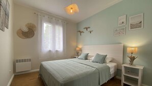 Quarto com cama grande, mesas de cabeceira com abajures, janela com cortinas e decorações nas paredes.