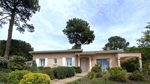 Uma casa de dois andares com telhado em telhas, uma entrada frontal com porta e uma grande árvore no quintal.