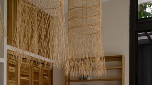 Une cuisine moderne avec un plan de travail blanc, des armoires en bois et un luminaire suspendu en fibres tressées.