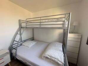 A bunk bed with a ladder, a bedside table with a lamp, and a white dresser.