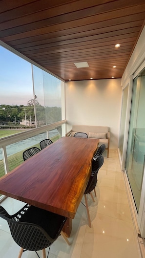 A modern dining area with a wooden table and chairs, a sofa, and a view of a river and greenery.