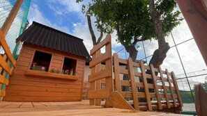 A wooden cabin with a sloped roof, a wooden fence, and a tree in the background.