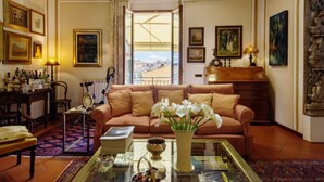 A living room with a sofa, a coffee table, a vase with flowers, a bookshelf, and a view through a glass door.
