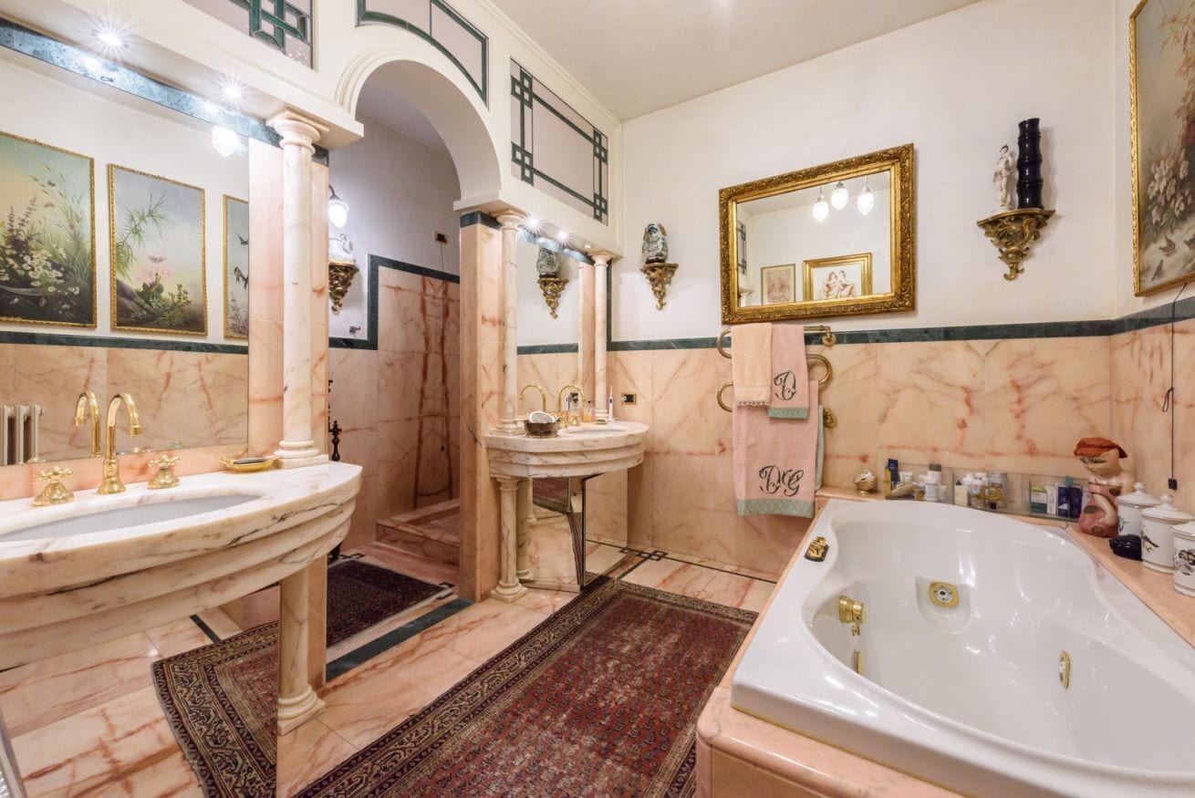 Une salle de bain luxueuse avec un sol en marbre, deux vasques, une baignoire et des appliques murales décoratives.