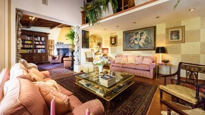A spacious living room with a fireplace, a large painting, and a bookshelf.