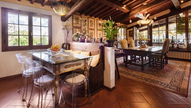 A dining area with a glass table, clear chairs, a wooden ceiling, and a large window.