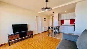 A modern living room with a flat-screen TV, a sofa, a dining area with chairs, and a kitchen with white cabinets. - QUIBERON - 2 rooms of about 38m² for 4 people SEA VIEW (QUIBERON)