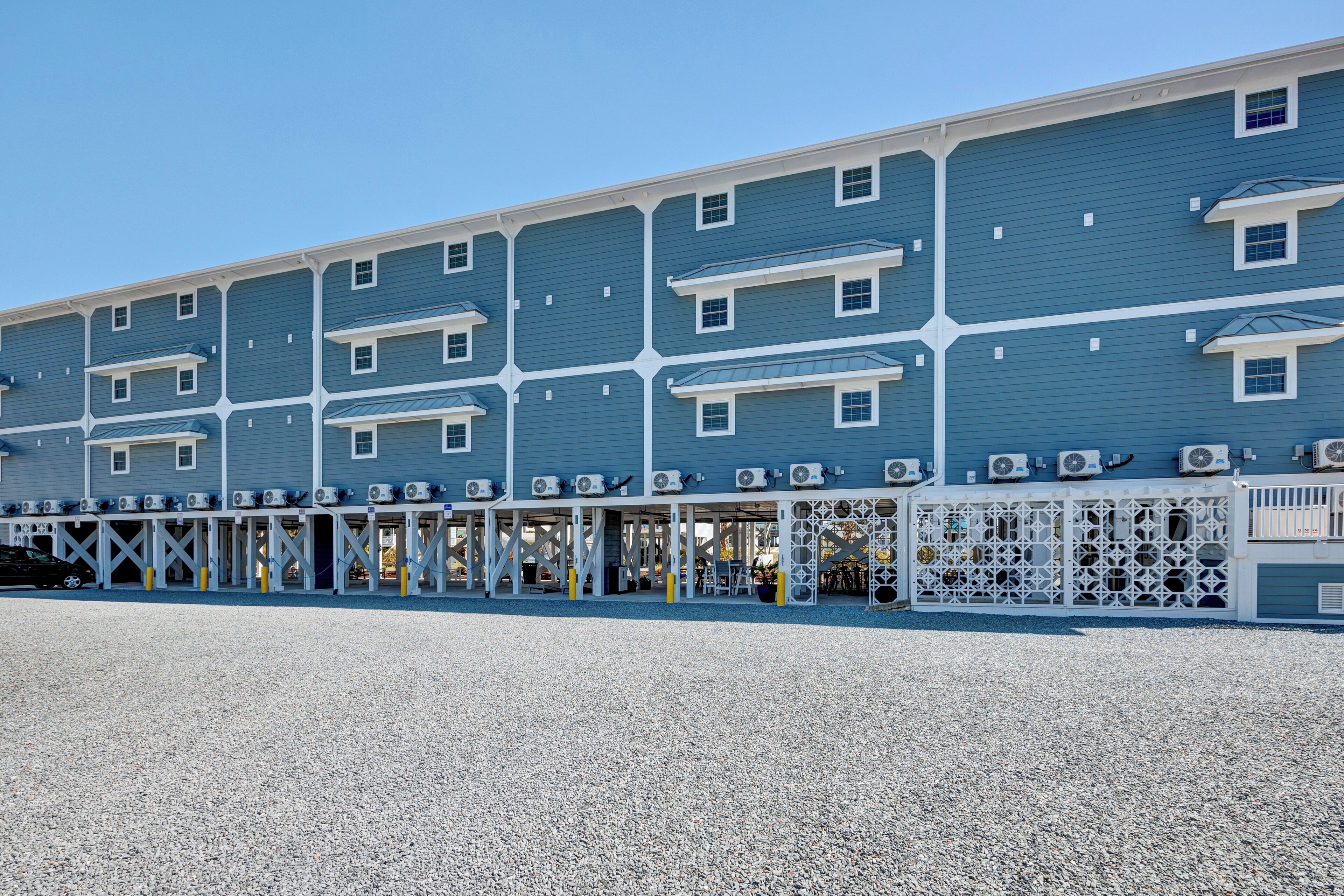 Un hôtel à plusieurs étages, à la façade bleue, doté de climatiseurs et d’un espace extérieur couvert aménagé avec des sièges.