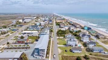Vue aérienne d’une zone résidentielle côtière, avec des maisons, une route et une plage.
