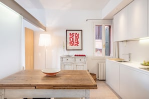 A modern kitchen with a wooden table, white cabinets, and a red abstract painting. - GuestHost - Studio located on the second floor of a building without a lift (you have to climb stairs to access it), able to accommodate up to 2 people.A few steps from the Clock Tower and Piazza dei Signori, in an enviable location. The apartment is fur (Padova)