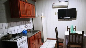 A compact kitchen with a gas stove, wooden cabinets, a sink, and a dining area with a table and chairs.