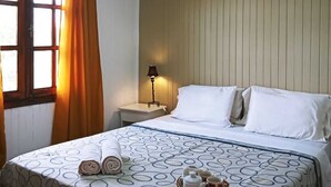 A hotel room with a bed, a nightstand, a lamp, a window with curtains, and a view of the outside.