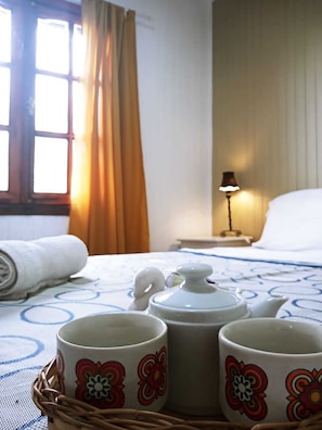 Ein Hotelzimmer mit einem Bett, einem Nachttisch mit Lampe und einem Korb mit drei Tassen mit Blumenmotiven.