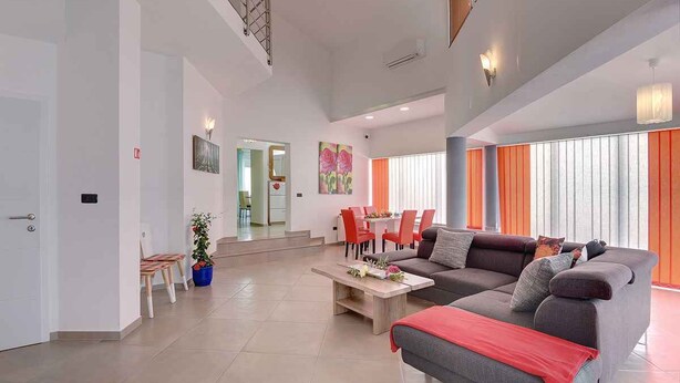 A spacious living room with a grey sofa, a coffee table, and a dining area with red chairs. - Villa mit Pool und Klimaanlage (Pula)
