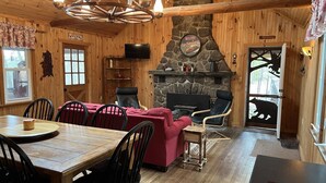 A cozy cabin interior with a wooden dining table, red sofa, and a fireplace.