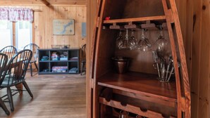 A wooden interior with a wine rack holding several glasses and bottles. There are wooden chairs and a table in the background.