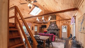 A wooden interior with a dining table, chairs, a fireplace, and a stone wall.