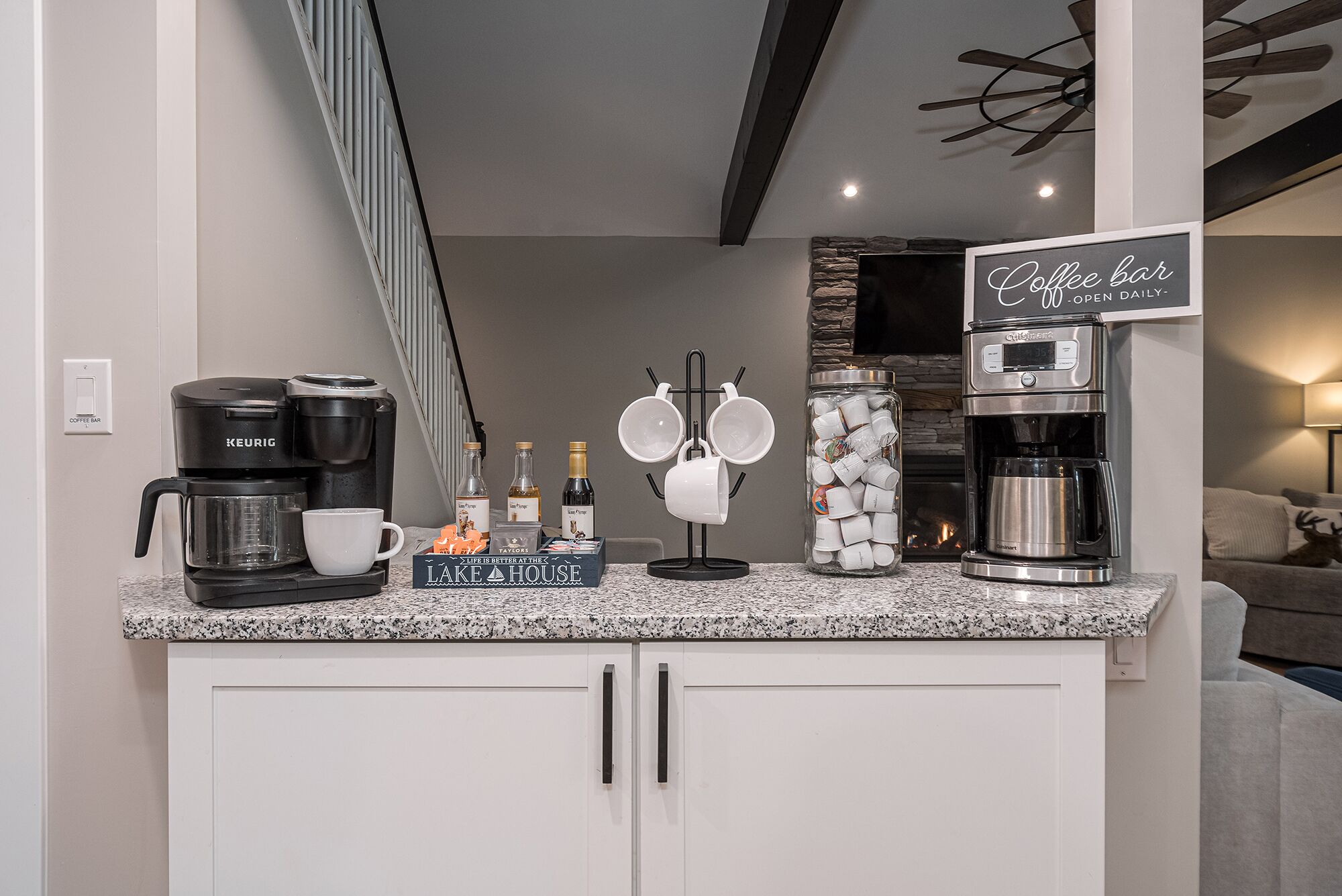 Una encimera de cocina con una cafetera, tazas y un cartel que indica barra de café.