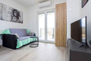 Een moderne woonkamer met een bank, een klein rond tafeltje, een televisie en een glazen schuifdeur naar een balkon.