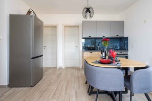 Een moderne keuken met een roestvrijstalen koelkast, grijze kastjes en een eethoek met een houten tafel en grijze stoelen.