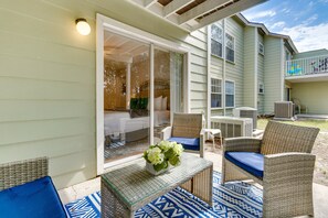 Une terrasse extérieure aménagée avec des meubles en osier, une table à plateau de verre ornée d’un vase de fleurs et un espace abrité offrant une vue sur la maison.