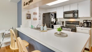 Una cocina moderna con armarios blancos, una isla grande, electrodomésticos de acero inoxidable y una silla de madera.