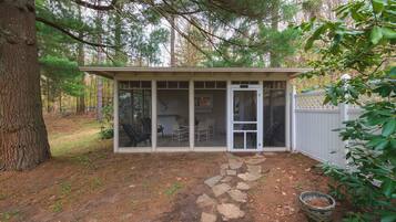 A small, single-story building with a glass door entrance, a patio area with outdoor furniture, and a stone pathway leading to the entrance.