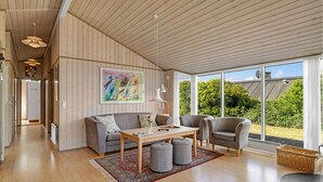 A spacious living room with a wooden floor, a grey sofa, a wooden coffee table, and a large window offering a view of greenery. - Gorgeous home in Allingåbro with WiFi (Allingåbro)