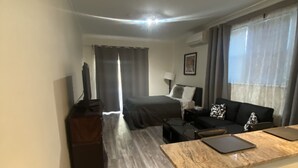 A modern hotel room with a bed, a seating area with a sofa and a small table, a television, and a desk with a laptop. - Beautifully Renovated DuPont Circle Studio (Washington)