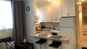 A compact kitchen with white cabinets, a stove, and a refrigerator. There are two bar stools at the counter. - Beautifully Renovated DuPont Circle Studio (Washington)