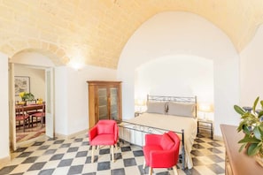 A bedroom with a checkered floor, a bed with a metal frame, two red chairs, and a wooden cabinet.