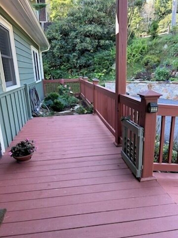 A wooden deck with a railing, a potted plant, and a stone wall in the background. - Higher Ground- Gated front porch, stunning views, one level, outdoor covered deck dining (Boone)