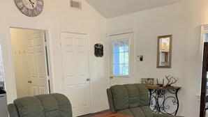 Una sala de estar con dos sillones verdes, una pequeña mesa de madera, un espejo decorativo y un reloj en la pared.