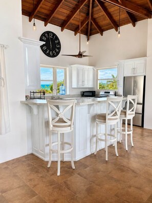 A kitchen with a central island, white cabinetry, a large clock, and a view of the ocean.