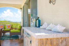 A balcony with a seating area, a bar counter, and a view of the sky.