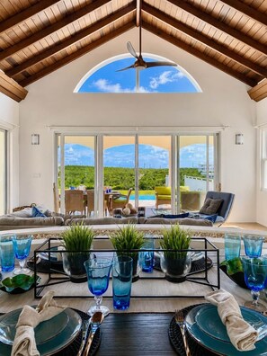 A dining area with a view of a pool and greenery, a ceiling fan, and a table set for a meal.