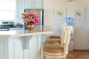 A kitchen with a marble countertop, a vase with flowers, a chair, and framed pictures on the wall.