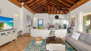 A spacious living area with a large TV, a wooden ceiling, and a view of the ocean.