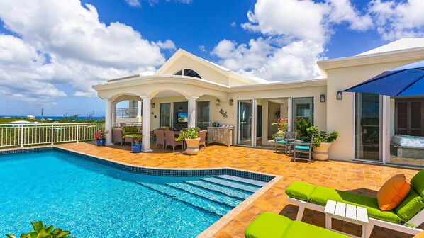 A poolside area with a swimming pool, outdoor seating, and a covered patio.