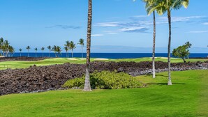 Een golfbaan met uitzicht op de oceaan, palmbomen en lava rotsen.